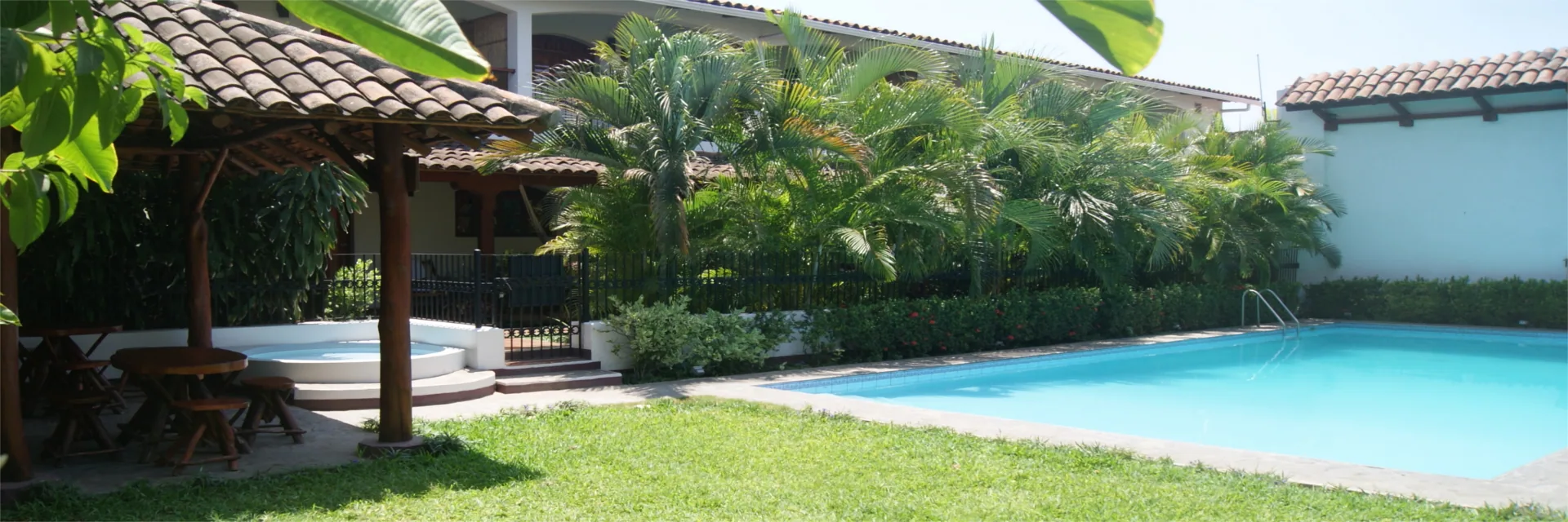 La piscina del hotel en el jardín, con palmeras y el rancho de sombra al fondo